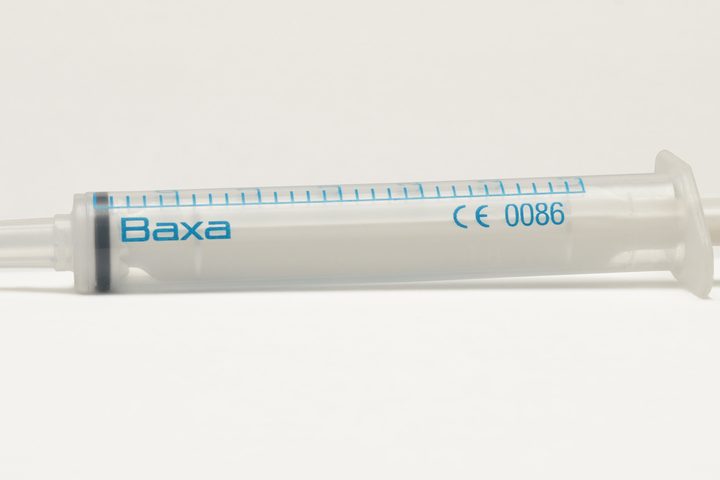 A clear graduated syringe lying across a dark ground, plunger drawn out, no needle fitted, the graduations and CE mark legible along the barrel.