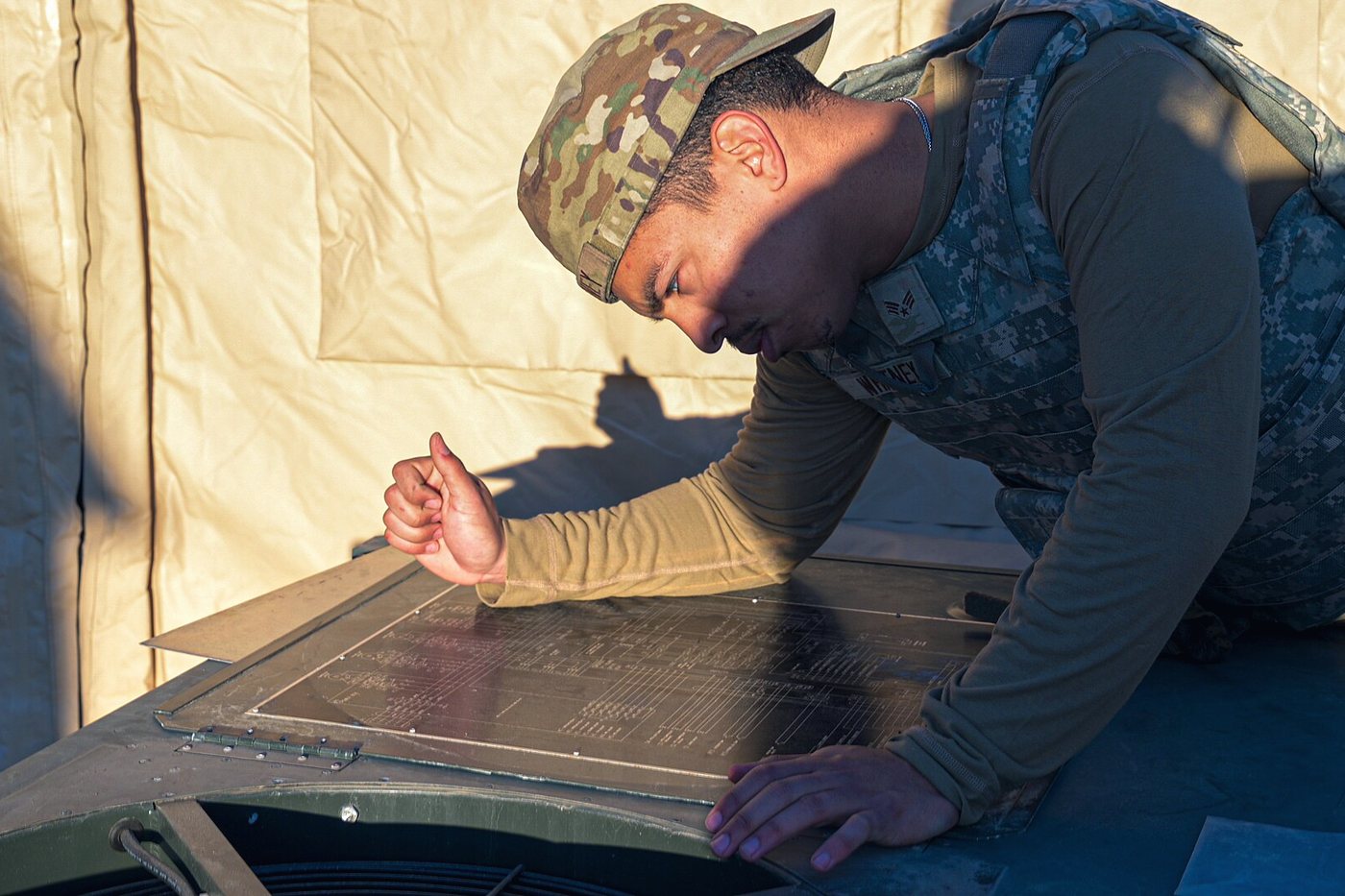 A technician kneeling over a pulled heat-exchanger panel, checking it in daylight