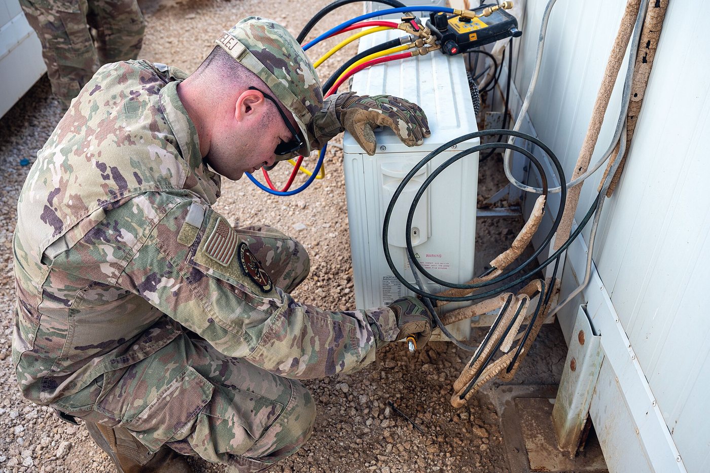 A technician kneeling beside a unit, making off the refrigerant line set
