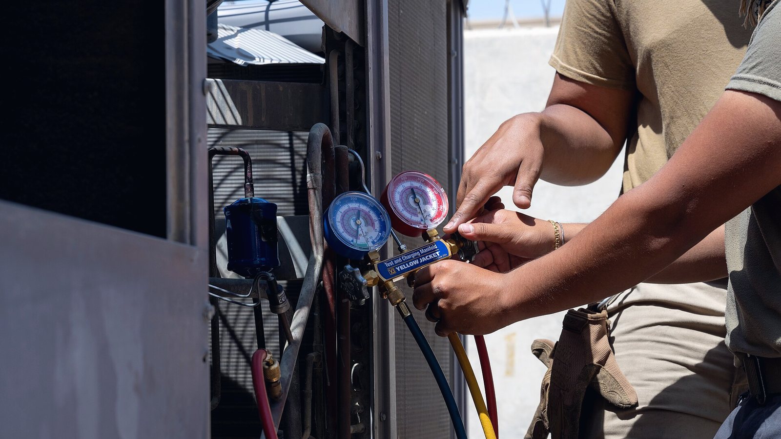 Two hands adjusting a refrigerant
manifold on the side of a unit — one gauge dial red, one blue