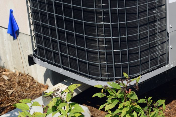 A residential air-conditioning condenser standing on its pad beside a house, plantings and mulch around the base